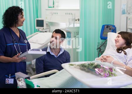 Doctor with medical chart making rounds, talking with couple in hospital room Stock Photo
