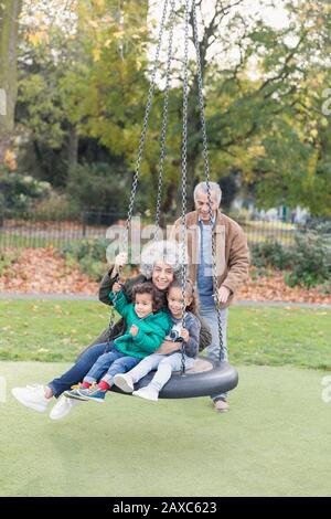 Grandparents and grandchildren playing on tire swing in park Stock Photo