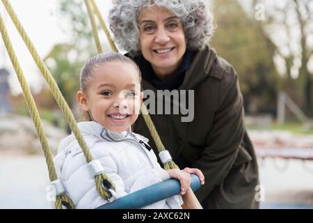 Portrait smiling grandmother and granddaughter playing on swing at playground Stock Photo