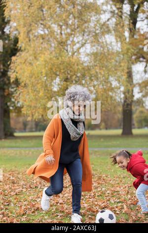 Playful grandmother playing soccer with granddaughter in autumn park Stock Photo