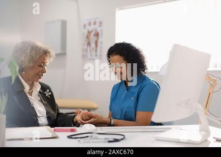 Female doctor examining hand of senior patient in doctors office Stock Photo