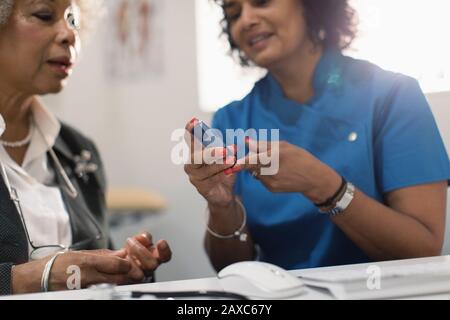 Female doctor teaching diabetic senior patient how to use glucometer Stock Photo
