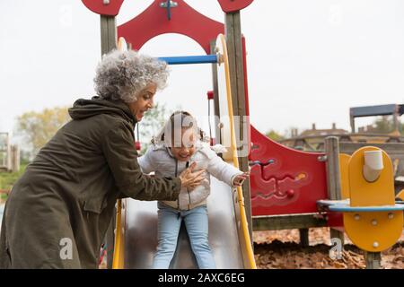 Grandmother playing with granddaughter on playground slide Stock Photo