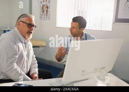 Male doctor meeting with senior patient at computer in doctors office Stock Photo