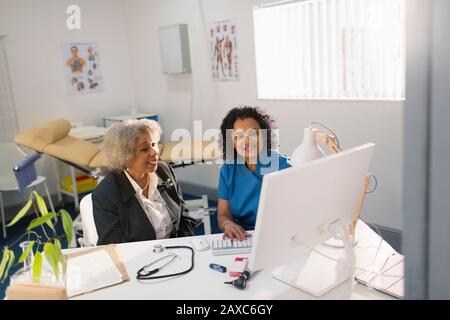 Female doctor meeting with senior patient at computer in doctors office Stock Photo
