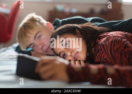 Teenage couple using smart phone, laying on bed Stock Photo