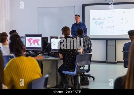 Junior high students at computers watching teacher at projection screen in classroom Stock Photo