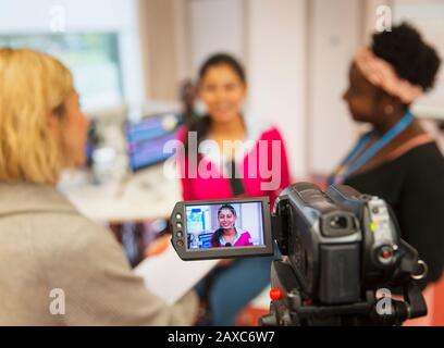 Video camera filming female community college journalism students in classroom Stock Photo