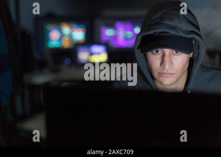 Male hacker in hoody using computer in dark room Stock Photo