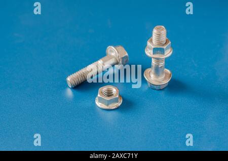 Two Bolts and nuts on a blue background.  Close-up nut with skirt and used bolt. Eye level shooting. Selective focus. Landscape photo arrangement. Stock Photo