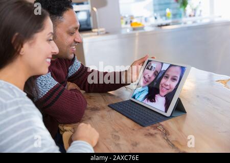 Couple video conferencing with daughters on digital tablet in kitchen Stock Photo
