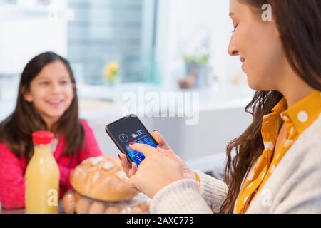 Daughter watching mother using smart phone in kitchen Stock Photo