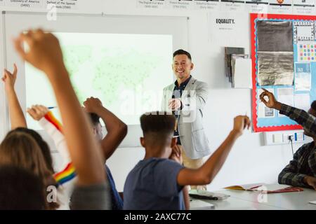 High school teacher leading lesson, calling on students with arms raised in classroom Stock Photo