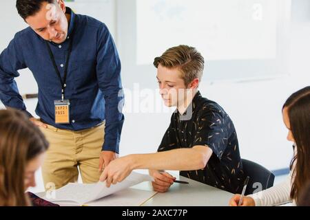 Male high school teacher helping boy student with homework in classroom Stock Photo