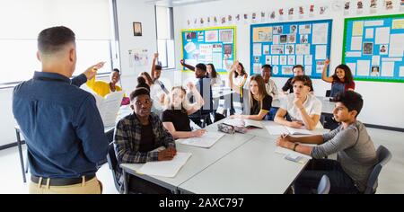 High school teacher calling on students with hands raised in classroom Stock Photo