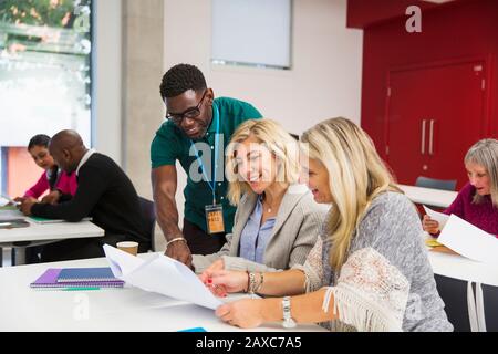 Community college instructor and students discussing paperwork in classroom Stock Photo