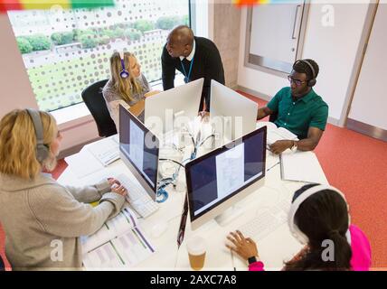 Community college instructor helping students with headphones using computers in computer lab Stock Photo