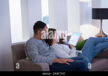 Couple relaxing, using digital tablet on living room sofa Stock Photo