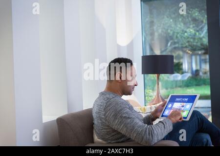 Man setting smart home alarm system from digital tablet on living room sofa Stock Photo