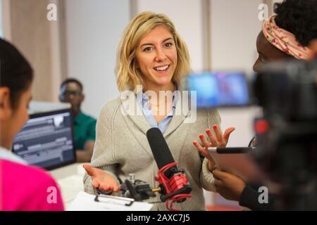Smiling, confident community college journalism students filming in classroom Stock Photo