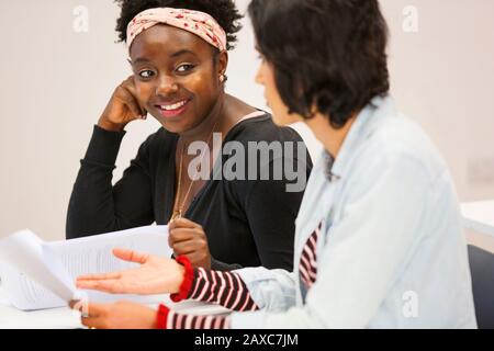 Smiling female community college students talking, discussing paperwork in classroom Stock Photo