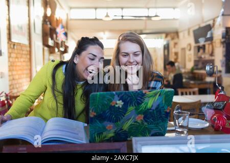 Happy, laughing young female college students using laptop in cafe window Stock Photo