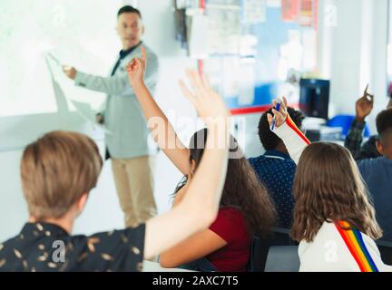 High school students with hands raised during lesson in classroom Stock Photo