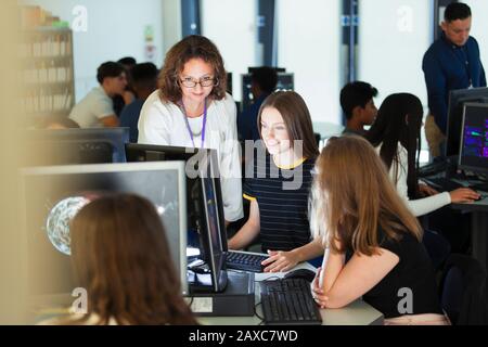 Female junior high teacher helping girl student at computer in computer lab Stock Photo