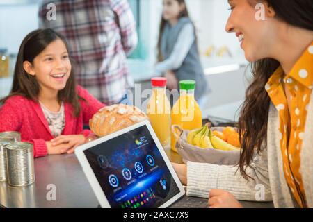 Mother and daughter talking, using digital tablet in kitchen Stock Photo