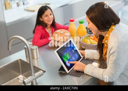 Daughter watching mother using digital tablet in kitchen Stock Photo