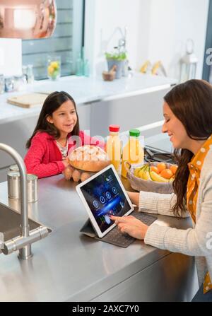 Daughter watching mother using digital tablet in kitchen Stock Photo