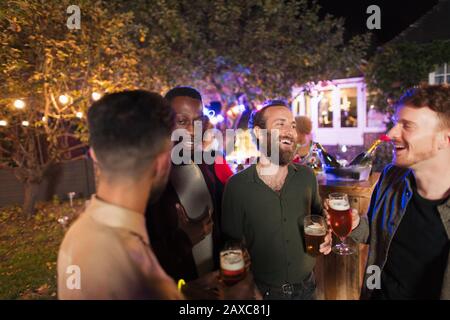 Male friends talking and drinking at garden party Stock Photo