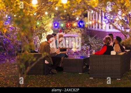 Friends talking and drinking under trees with string lights at garden party Stock Photo