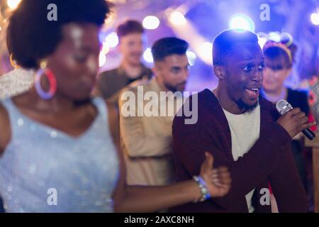 Friends signing karaoke and dancing at party Stock Photo
