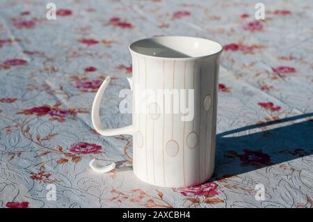 White porcelain milk mug with broken handle closeup on covered table Stock Photo