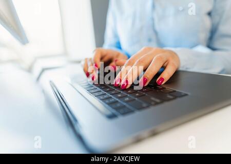 Female hands with bright manicure are typing on a laptop keyboard Stock Photo