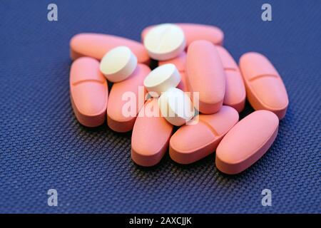 Large pink oval-shaped tablets and small white round tablets. Pills against a blue background. Vitamin D3 in pills. Stock Photo