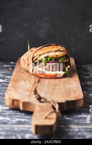 A large mouth-watering burger with grilled beef patty and fresh vegetables. Tasty american cheeseburger on a wooden board. Classic homemade burger in