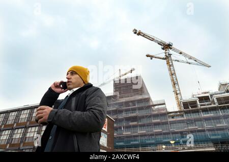 A man with a coffee mug paper cup in his hand talking on a mobile phone Stock Photo