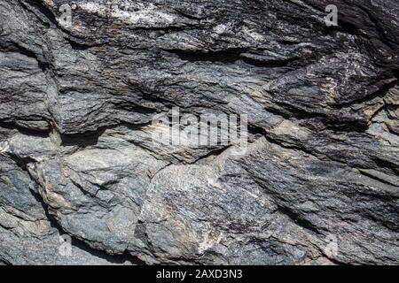 Grey black granite stone on natural wall in mountains. Close up gray texture, rough surface material. For design, web Stock Photo