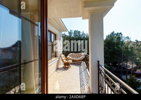 Large beautiful rich spacious veranda in the cottage with views of the mountains and the sea. Soft summer wicker sofas and armchairs. Veranda with bea Stock Photo