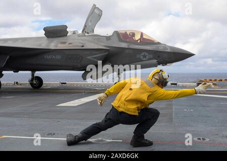 A U.S. Navy flight handler signals a Marine Corps F-35B Lightning II stealth fighter aircraft assigned to the 31st Marine Expeditionary Unit for ake off from the flight deck of the amphibious assault ship USS America February 6, 2020 in the Philippine Sea. Stock Photo
