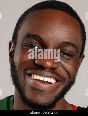 Close up portrait of a young african american happily smiling positively with beautiful teeth and looking at straight on a grey background Stock Photo