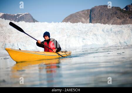 Young man wearing sunglasses and kayaking in icy waters Stock Photo