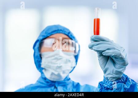 Medic in hazmat protective suit holds a test tube with a coronavirus positive blood sample from Wuhan, China. 2019 nCoV pandemic. stop coronavirus Stock Photo