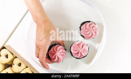 Chocolate cupcakes with raspberry buttercream frosting, and heart shaped cookies close up on white background, top view. Stock Photo