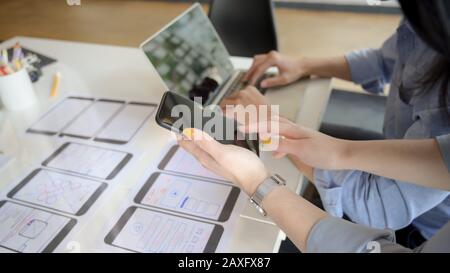 Close-up view of young female UI designer showing smartphone to her co-worker for the project Stock Photo