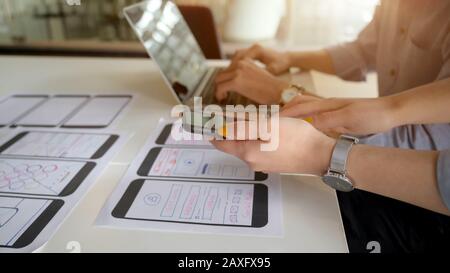 Close-up view of young female UI designer showing smartphone to her co-worker for the project Stock Photo