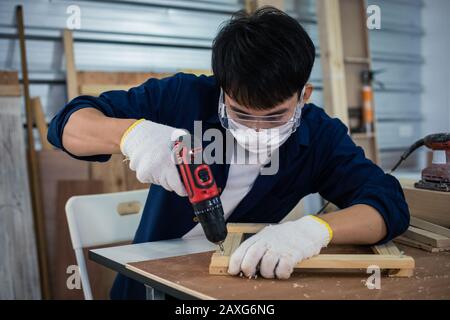 Asian man Carpenter working with technical drawing or blueprint construction paper lying on a workshop with carpentry tools and wood at home Stock Photo