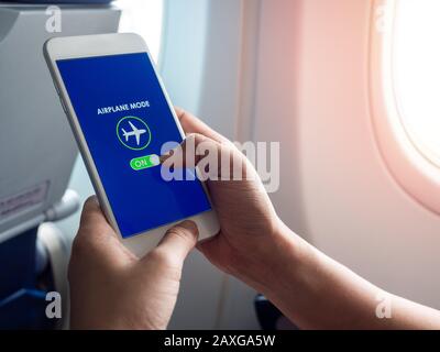 Flight mode concept. Hand holding white smartphone and turned on airplane mode on screen near the window on the airplane with copy space. Stock Photo